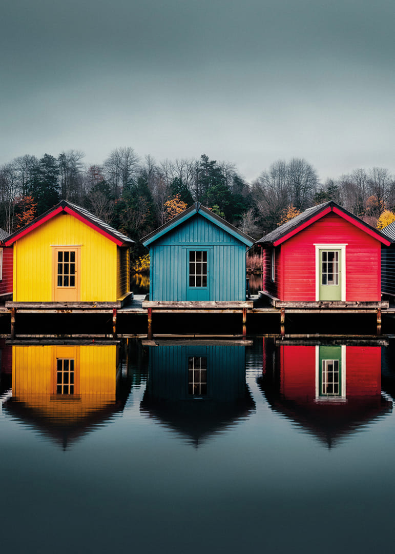 Three colorful houses are reflected in calm water, creating harmony.-12