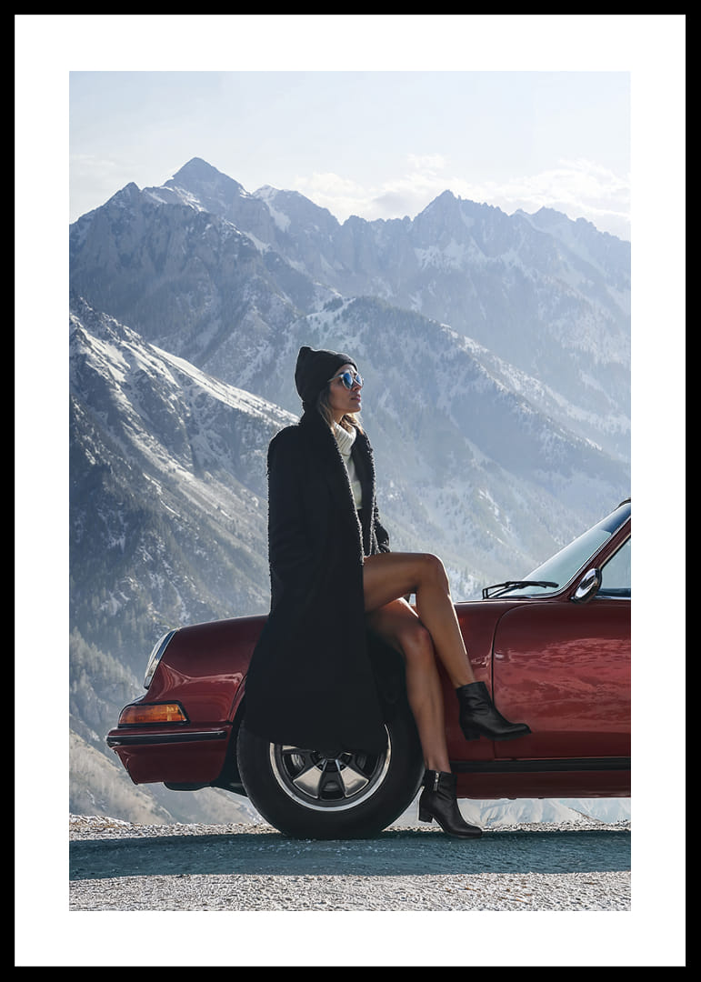 A stylish woman leans against a car with mountains in the background.-12