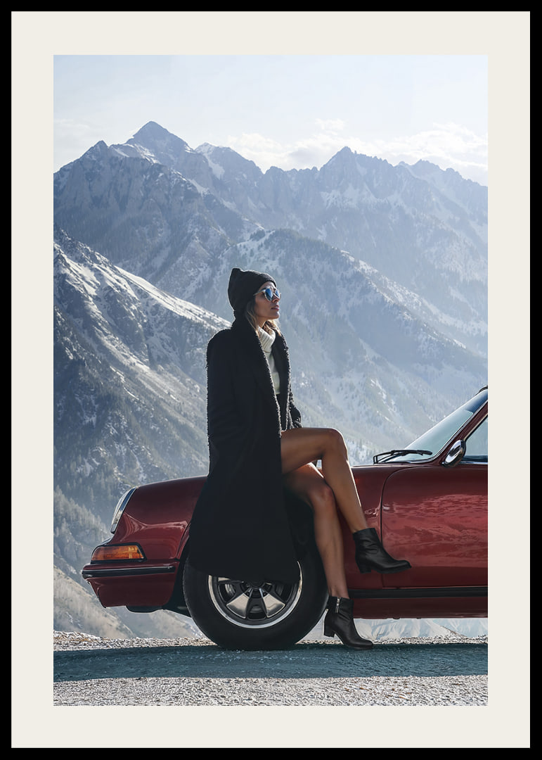 A stylish woman leans against a car with mountains in the background.-12