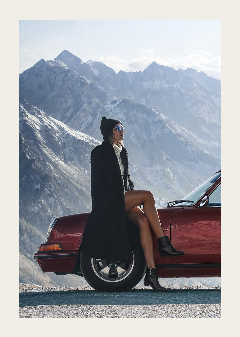 Une femme élégante est appuyée contre une voiture, avec des montagnes en arrière-plan.-12