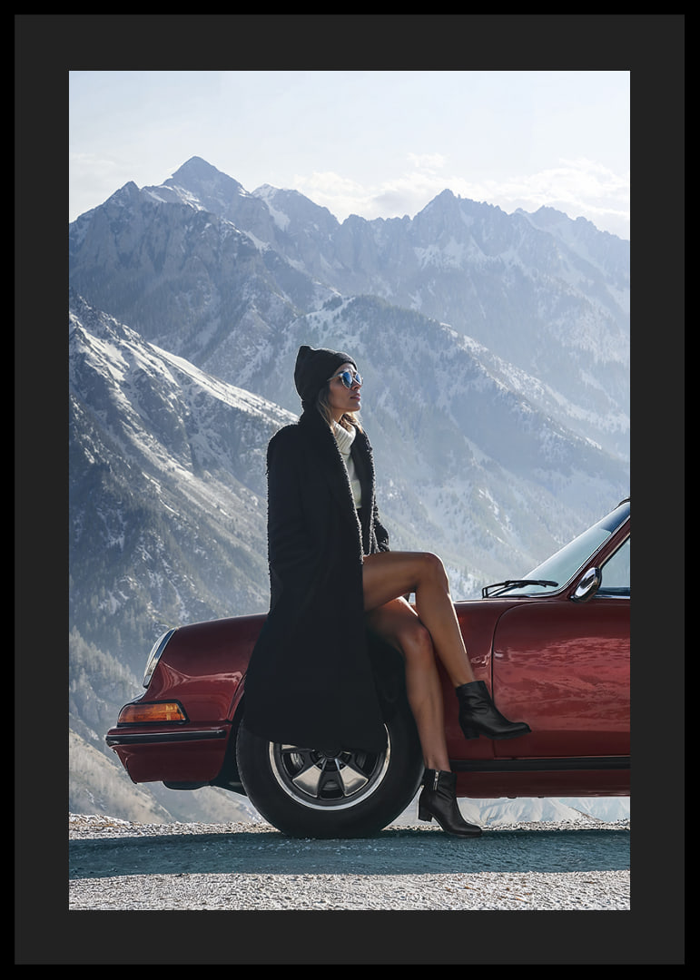 A stylish woman leans against a car with mountains in the background.-12