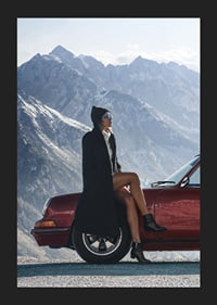 A stylish woman leans against a car with mountains in the background.-5