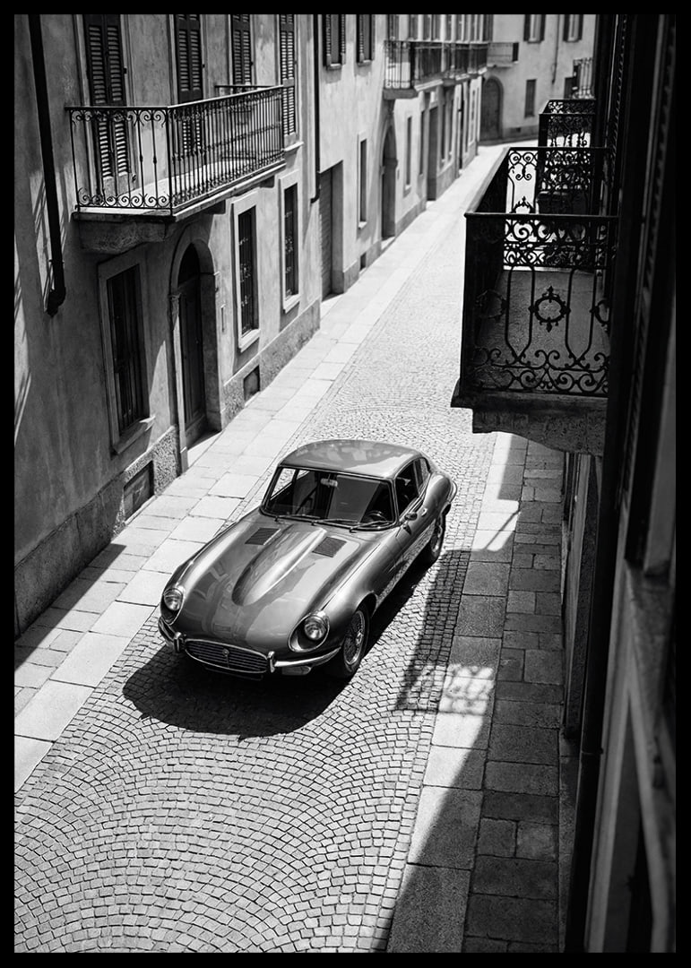 En klassisk Jaguar E-Type majestätiskt på en solbelyst stenlagd gata.-12