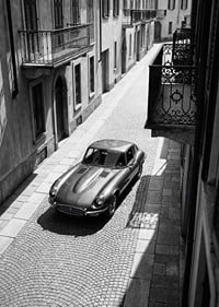 En klassisk Jaguar E-Type majestätiskt på en solbelyst stenlagd gata.-7