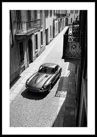 En klassisk Jaguar E-Type majestätiskt på en solbelyst stenlagd gata.-0