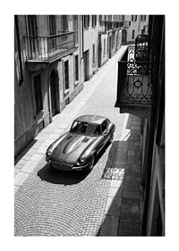 En klassisk Jaguar E-Type majestätiskt på en solbelyst stenlagd gata.-1