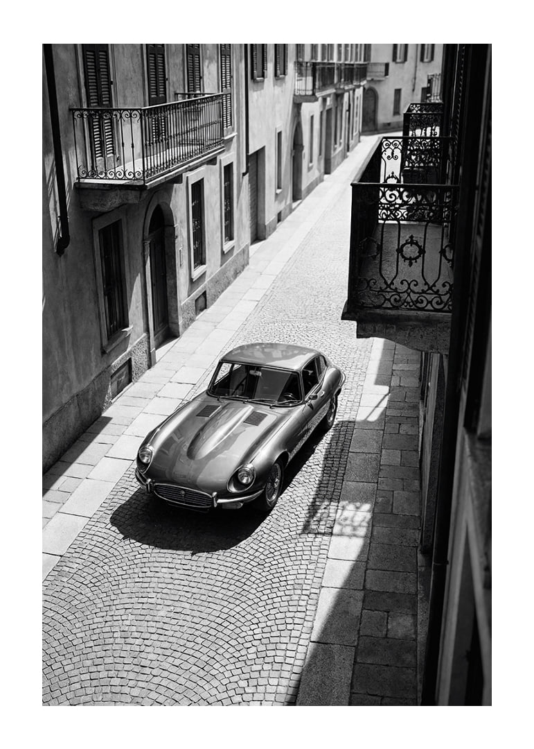 En klassisk Jaguar E-Type majestätiskt på en solbelyst stenlagd gata.-12