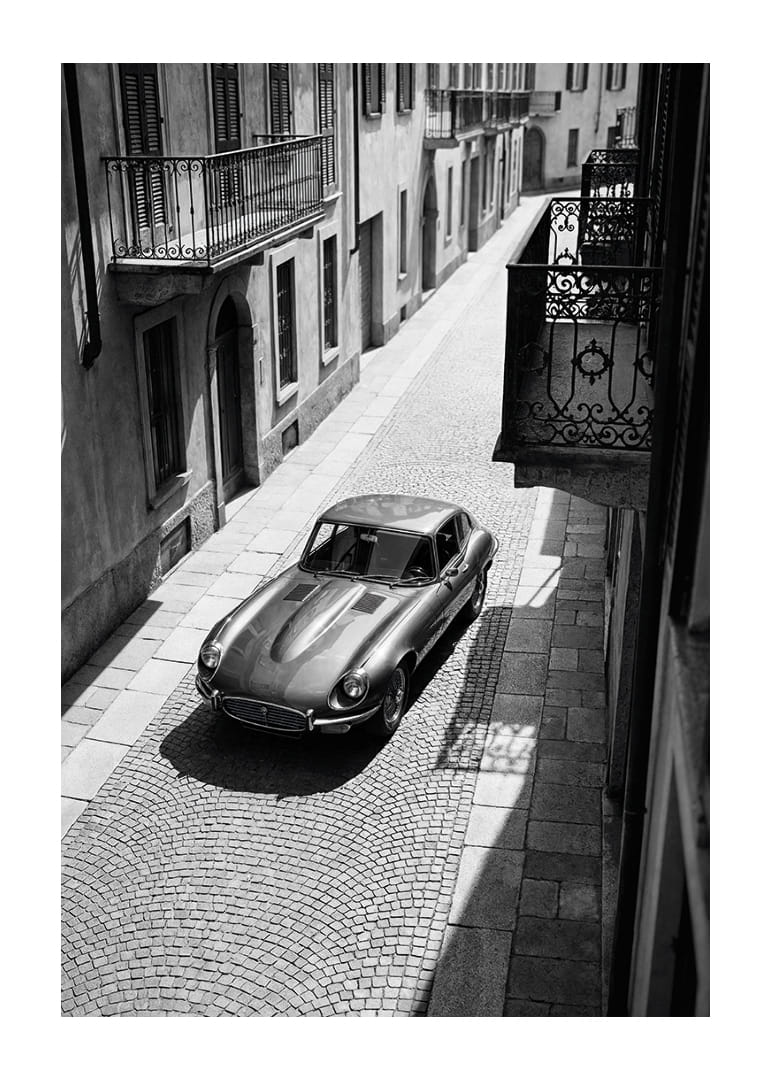 A classic Jaguar E-Type majestically stands on a sunlit cobblestone street.-12