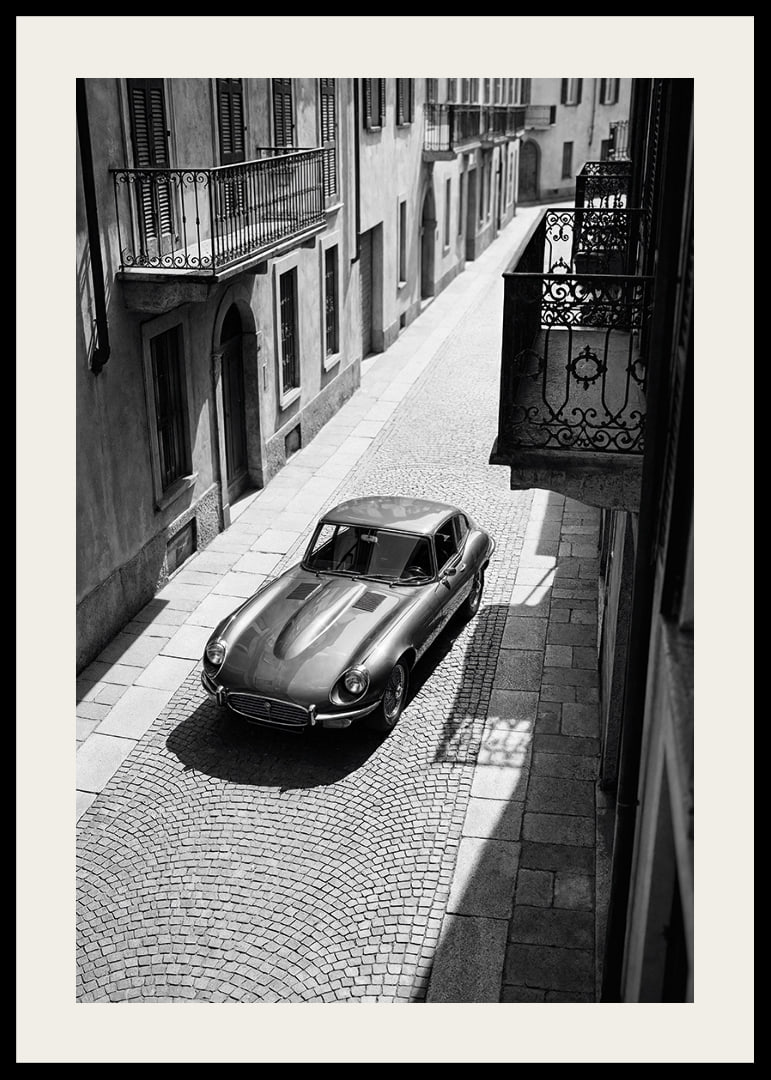 En klassisk Jaguar E-Type majestätiskt på en solbelyst stenlagd gata.-12