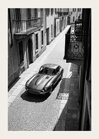 En klassisk Jaguar E-Type majestätiskt på en solbelyst stenlagd gata.-3