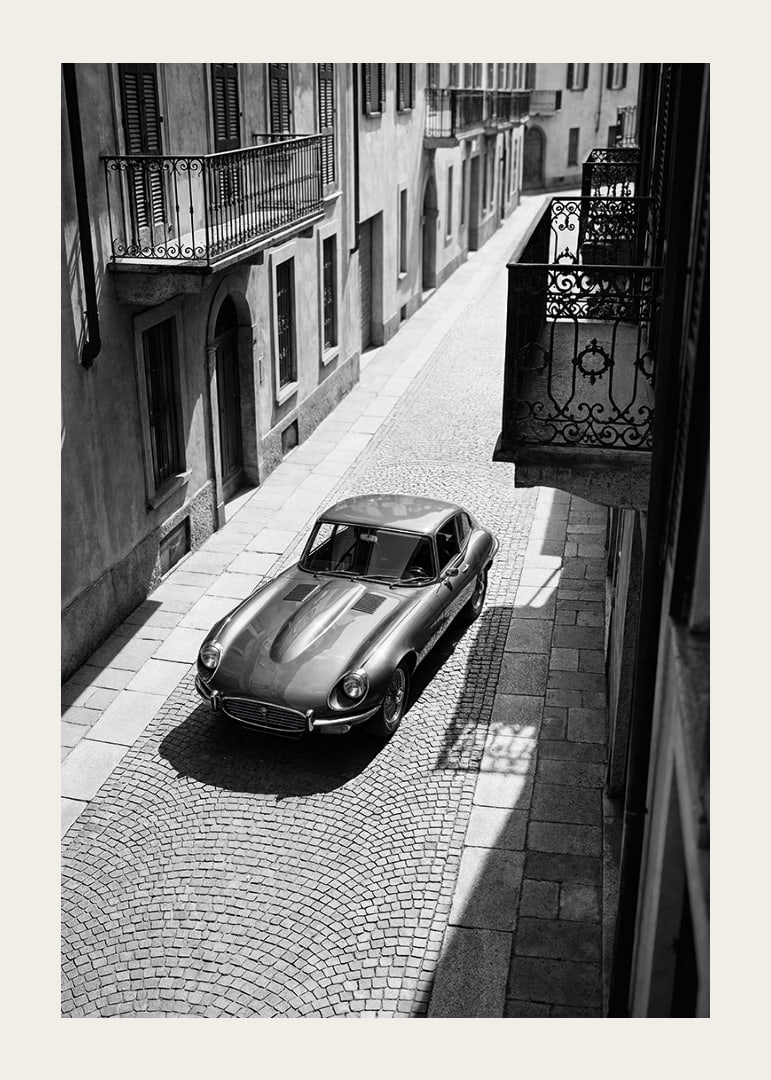En klassisk Jaguar E-Type majestätiskt på en solbelyst stenlagd gata.-12
