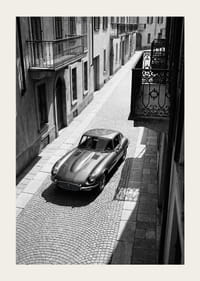 En klassisk Jaguar E-Type majestätiskt på en solbelyst stenlagd gata.-3