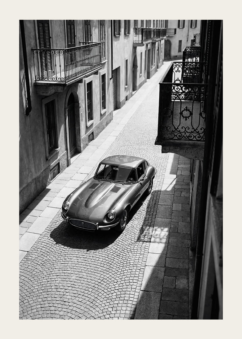 En klassisk Jaguar E-Type majestätiskt på en solbelyst stenlagd gata.-12