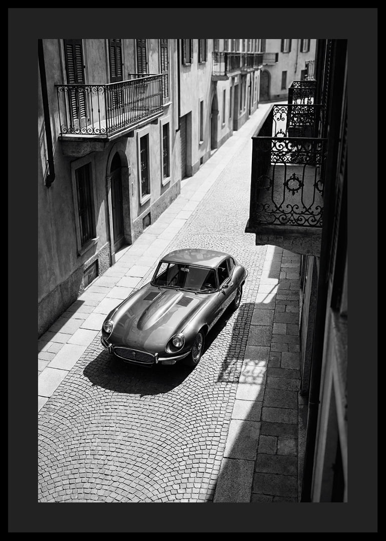 En klassisk Jaguar E-Type majestätiskt på en solbelyst stenlagd gata.-12