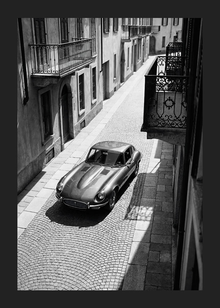 En klassisk Jaguar E-Type majestätiskt på en solbelyst stenlagd gata.-12