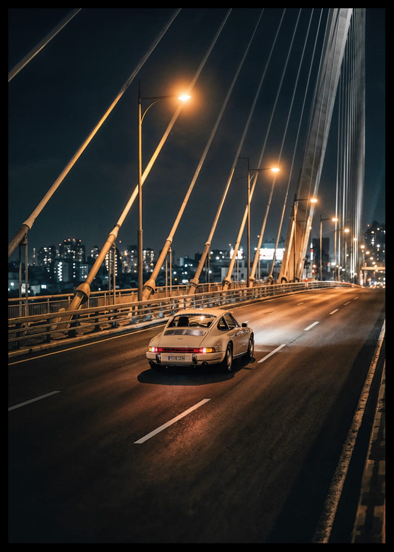 Clásico Porsche 911 en un puente iluminado hacia la ciudad por la noche.-12