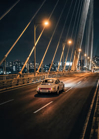 Clásico Porsche 911 en un puente iluminado hacia la ciudad por la noche.-3