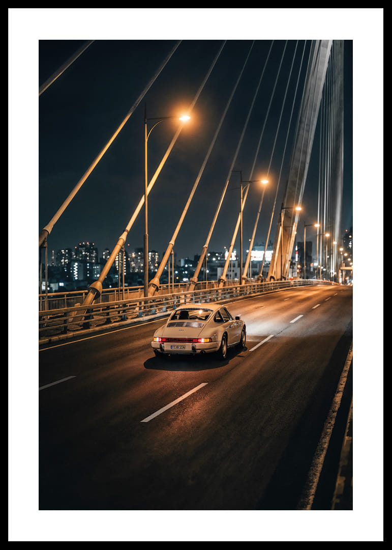 Clásico Porsche 911 en un puente iluminado hacia la ciudad por la noche.-12