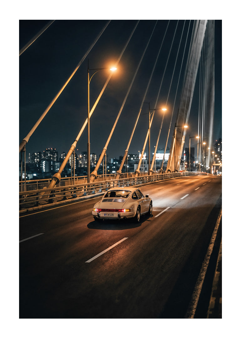 Porsche 911 clasic pe un pod iluminat spre oraș noaptea.-12