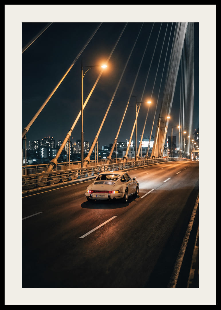 Classic Porsche 911 on an illuminated bridge towards the city at night.-12