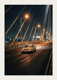 Classic Porsche 911 on an illuminated bridge towards the city at night.-3