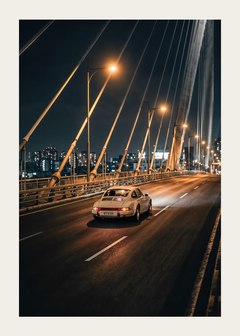 Classic Porsche 911 on an illuminated bridge towards the city at night.-12