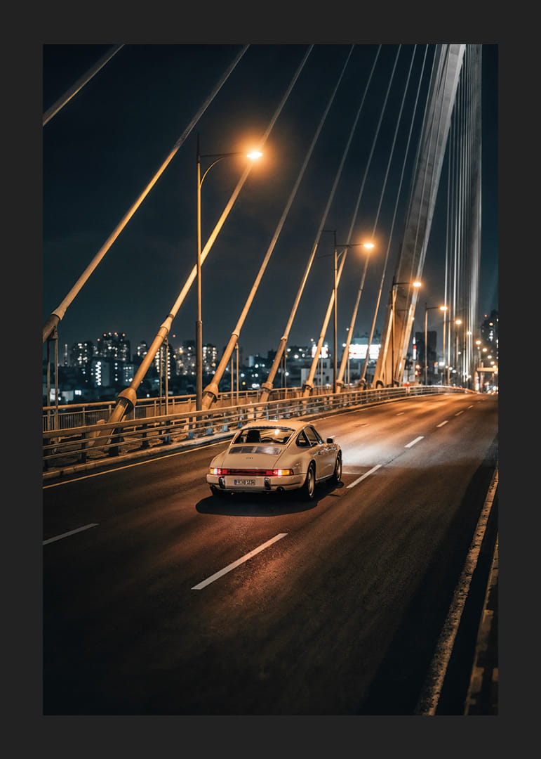 Classic Porsche 911 on an illuminated bridge towards the city at night.-12