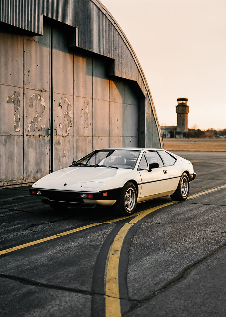 Elegants klasiskais Lotus Esprit rūpniecības ēkas priekšā saulrietā.-12