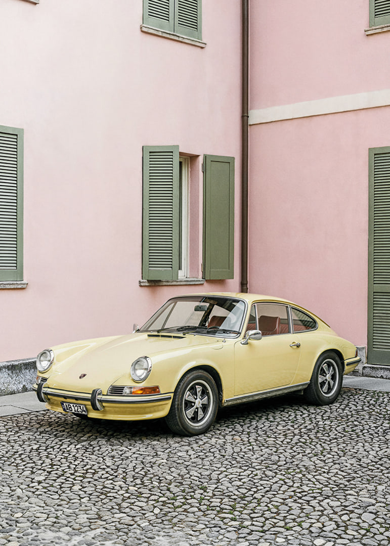 A charming pastel yellow Porsche 911 in front of a pink wall gives a retro feel.-12