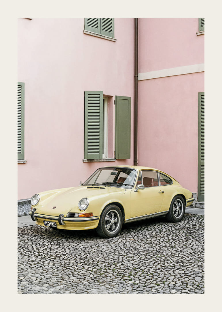 A charming pastel yellow Porsche 911 in front of a pink wall gives a retro feel.-12