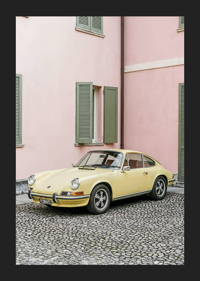 A charming pastel yellow Porsche 911 in front of a pink wall gives a retro feel.-12