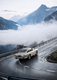 En klassisk Aston Martin DB5 färdas genom dimmiga berg på en slingrande väg.-7