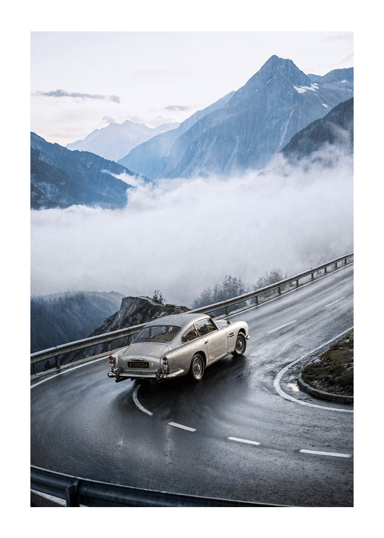 En klassisk Aston Martin DB5 färdas genom dimmiga berg på en slingrande väg.-12
