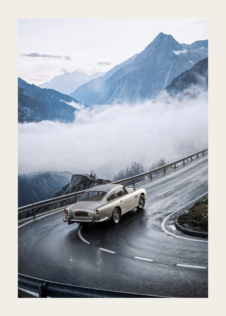 En klassisk Aston Martin DB5 färdas genom dimmiga berg på en slingrande väg.-12