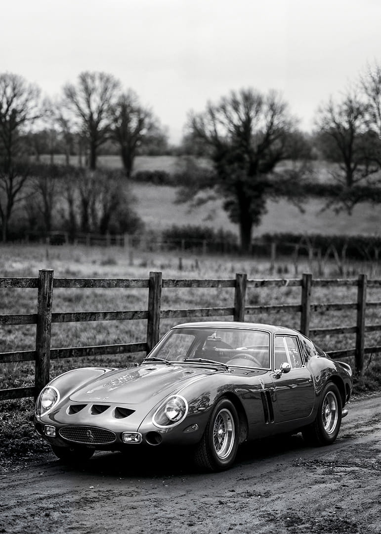 En klassisk Ferrari 250 GTO står ståtlig på en grusväg omgiven av träd.-12