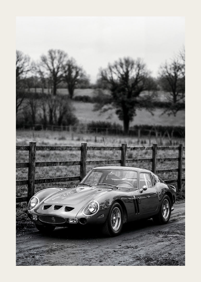 En klassisk Ferrari 250 GTO står ståtlig på en grusväg omgiven av träd.-12