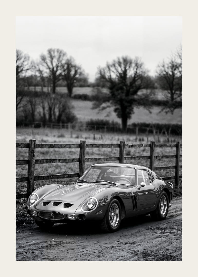 En klassisk Ferrari 250 GTO står ståtlig på en grusväg omgiven av träd.-12