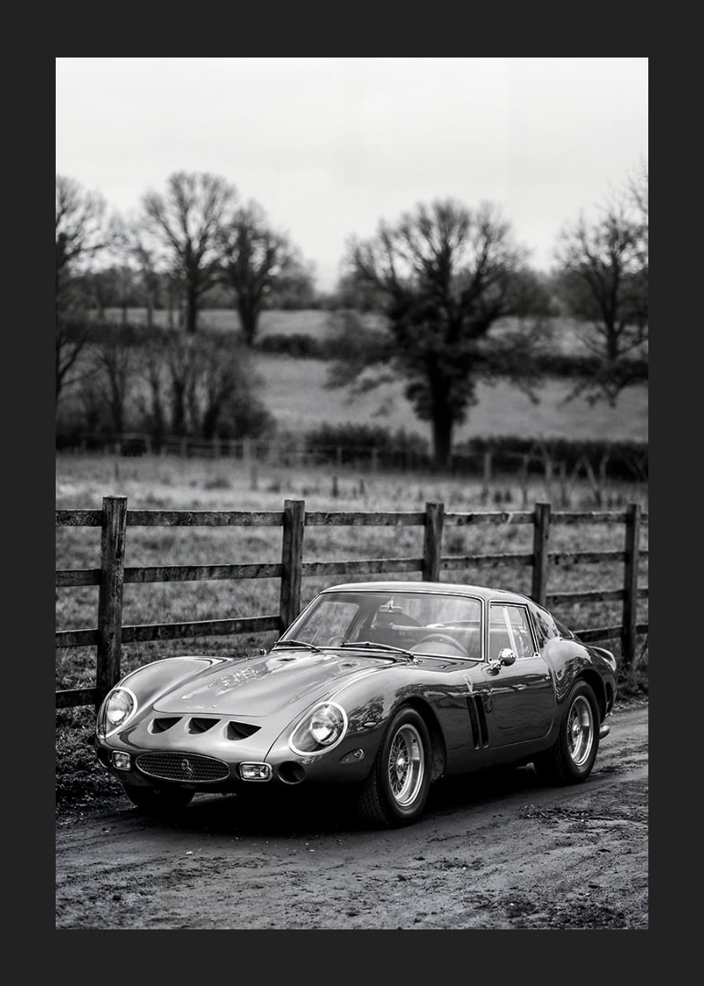 En klassisk Ferrari 250 GTO står ståtlig på en grusväg omgiven av träd.-12