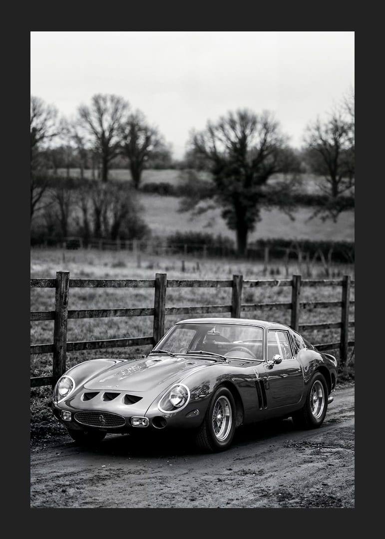 En klassisk Ferrari 250 GTO står ståtlig på en grusväg omgiven av träd.-12