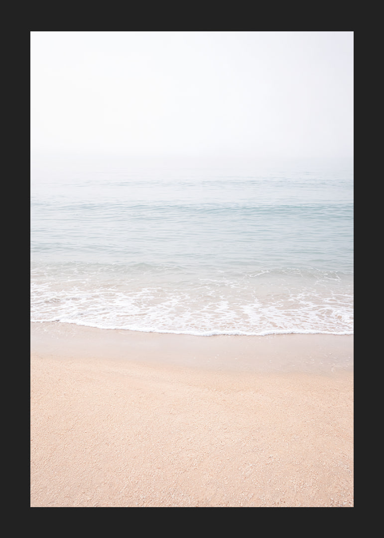 A misty coast where the sea meets the sand in soft tones.-12