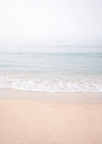 A misty coast where the sea meets the sand in soft tones.-7