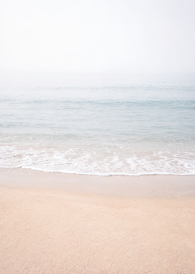 A misty coast where the sea meets the sand in soft tones.-12