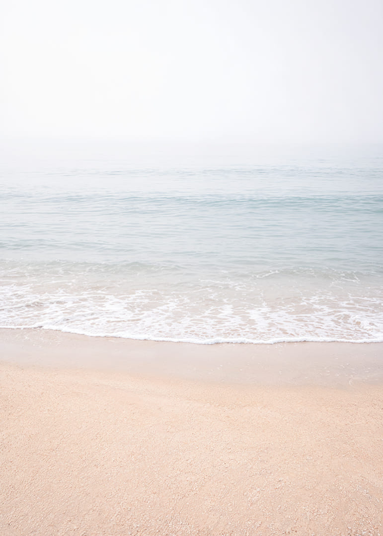 A misty coast where the sea meets the sand in soft tones.-12