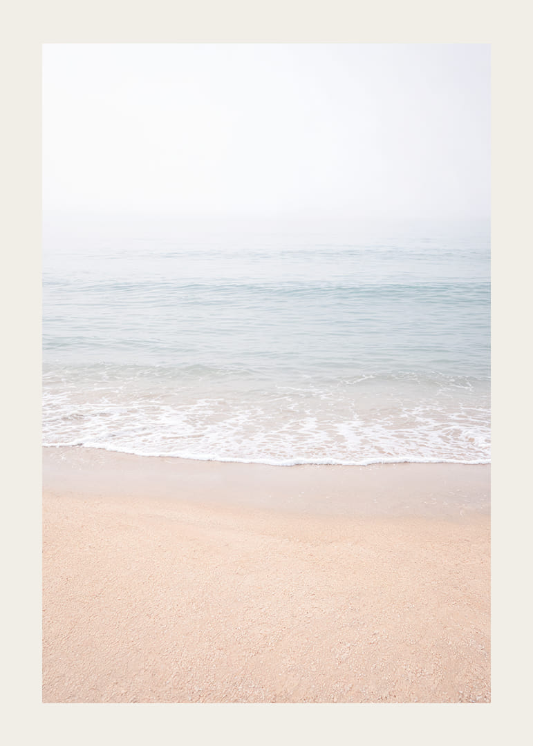 A misty coast where the sea meets the sand in soft tones.-12