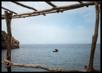 A lone boat rests under a clear blue sky in the arms of the ocean.-6