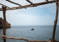 A lone boat rests under a clear blue sky in the arms of the ocean.-7