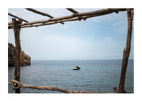 A lone boat rests under a clear blue sky in the arms of the ocean.-1