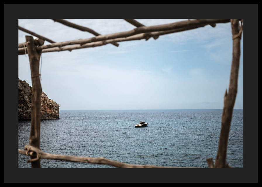 A lone boat rests under a clear blue sky in the arms of the ocean.-12