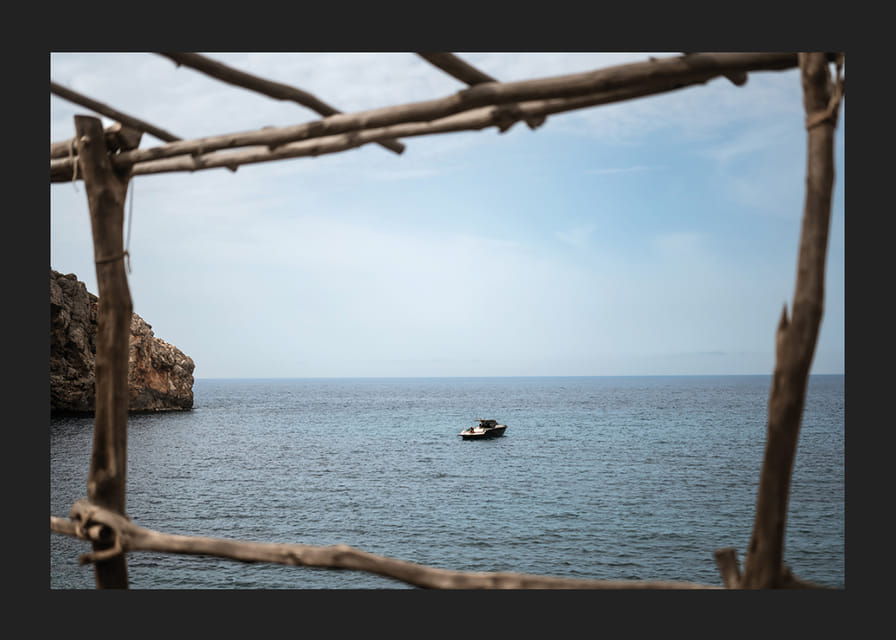 A lone boat rests under a clear blue sky in the arms of the ocean.-12