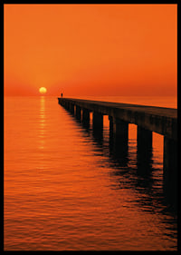 A lone person on a pier in a glowing orange sunset light.-6